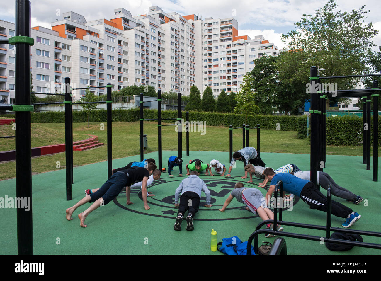 Bremen, Germany. 06th June, 2017. Coach Sergej Rossel (green shirt in the background) works out with youths and young adults on the grounds of an outdoor training facility in the district Osterholz-Tenever in Bremen, Germany, 06 June 2017. Work out to reduce stress, the 'Hood-Training' is being offered by the Bremen project to kids and youths from socially disadvantaged backgrounds. The project is being rewarded by the German Chancellor in Berlin on the 7th June 2017. Photo: Ingo Wagner/dpa/Alamy Live News Stock Photo