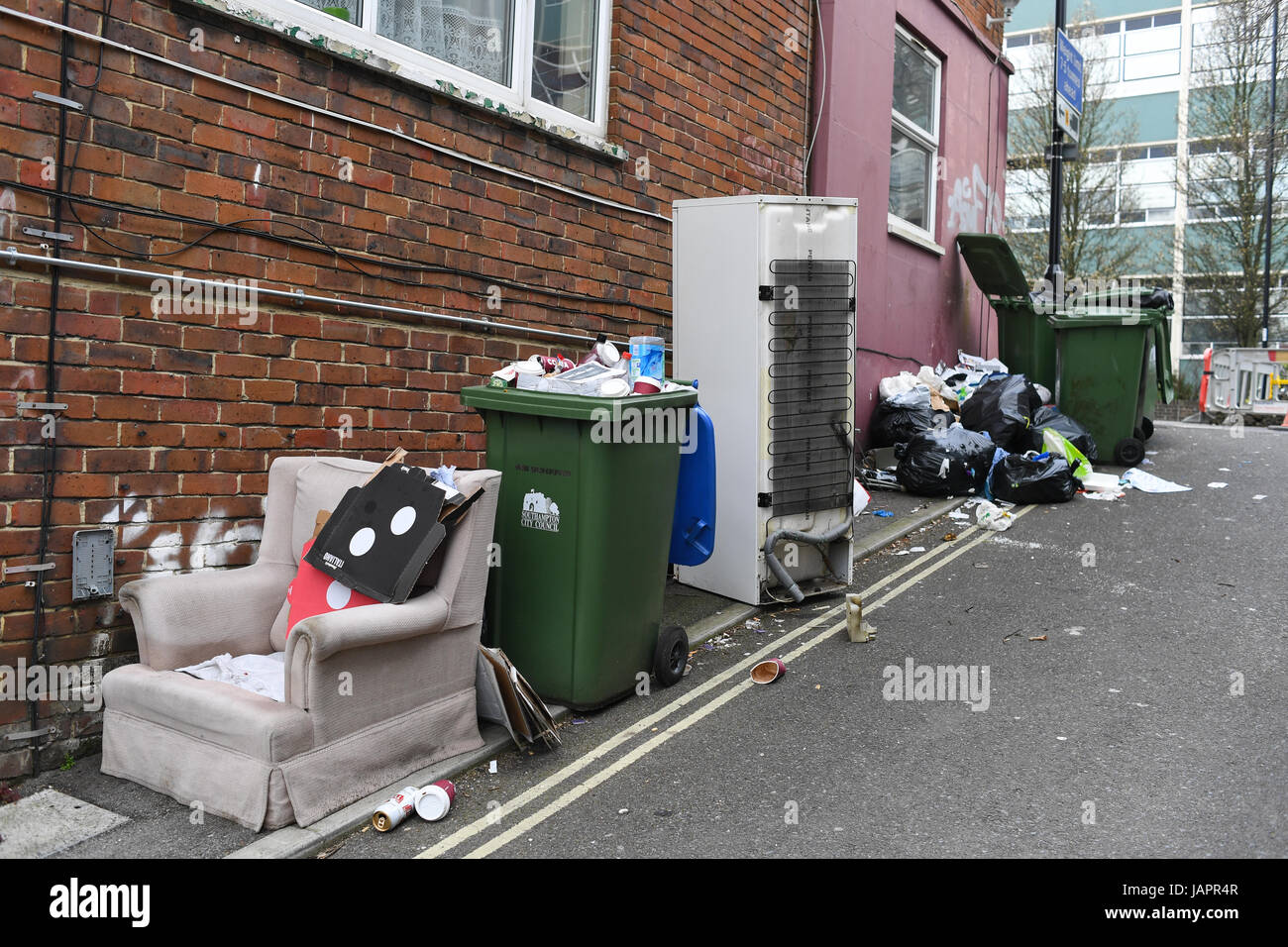 Rubbish overflowing and dumped at roadside, including a fridge freezer and chair. Stock Photo