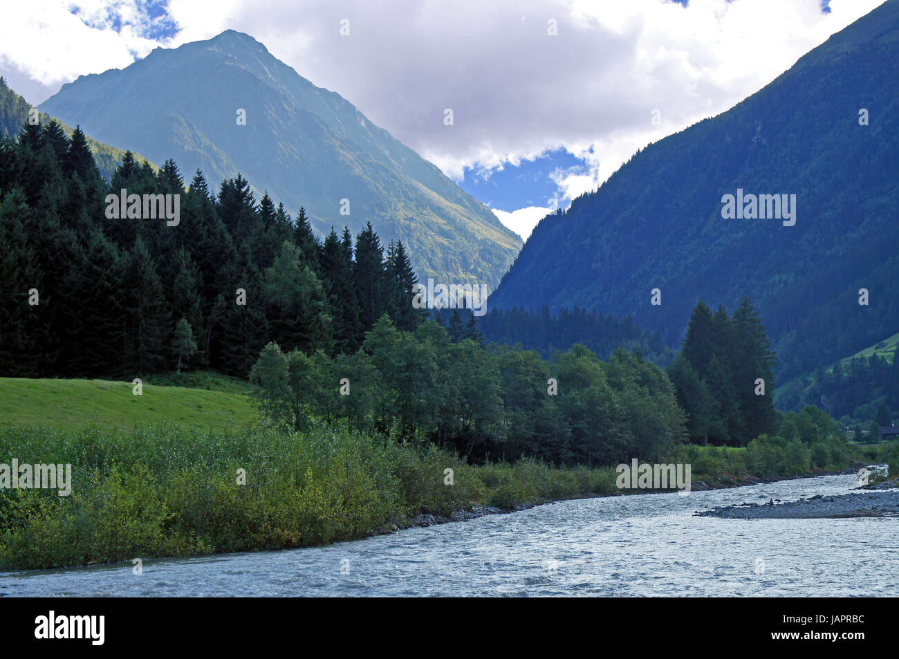 Ein Tal mit einem breiten Bach, Wiesen und bewaldete Berge in Tirol A valley with a wide creek, meadows and forested mountains in Tyrol Stock Photo
