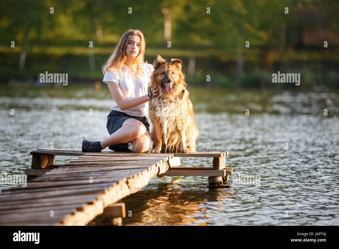 Teenage girl in white shirt with her dog sitting on pathway in the park ...