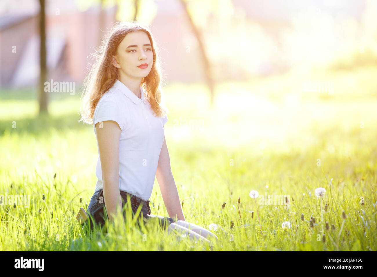 Young teenage girl sitting on green grass in sunny park. Image with copy space aside Stock Photo