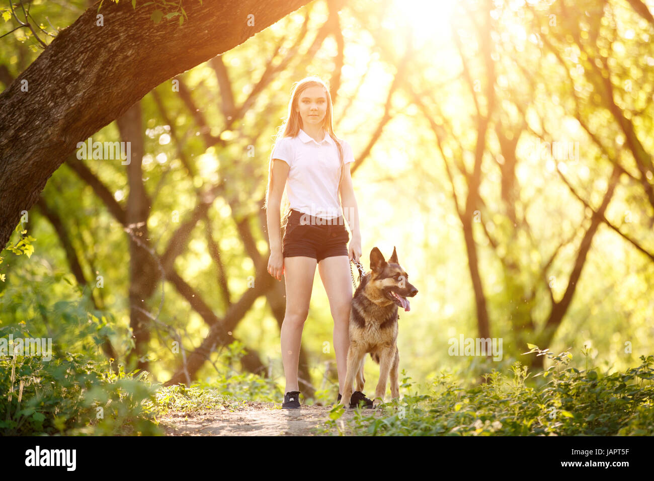 Teenage girl in white shirt with her dog sitting on pathway in the park ...