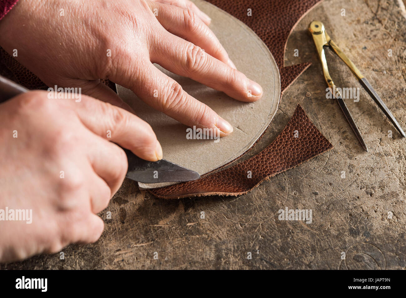 Shoemaker, hands cutting with template and knife a piece of leather on work table, Kainisch, Styria, Austria Stock Photo
