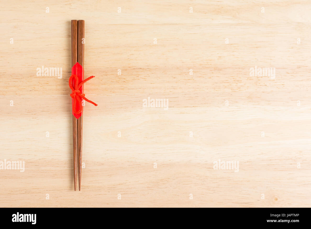 Japanese wooden chopsticks wrapped in red paper and red rope on wooden table. Stock Photo