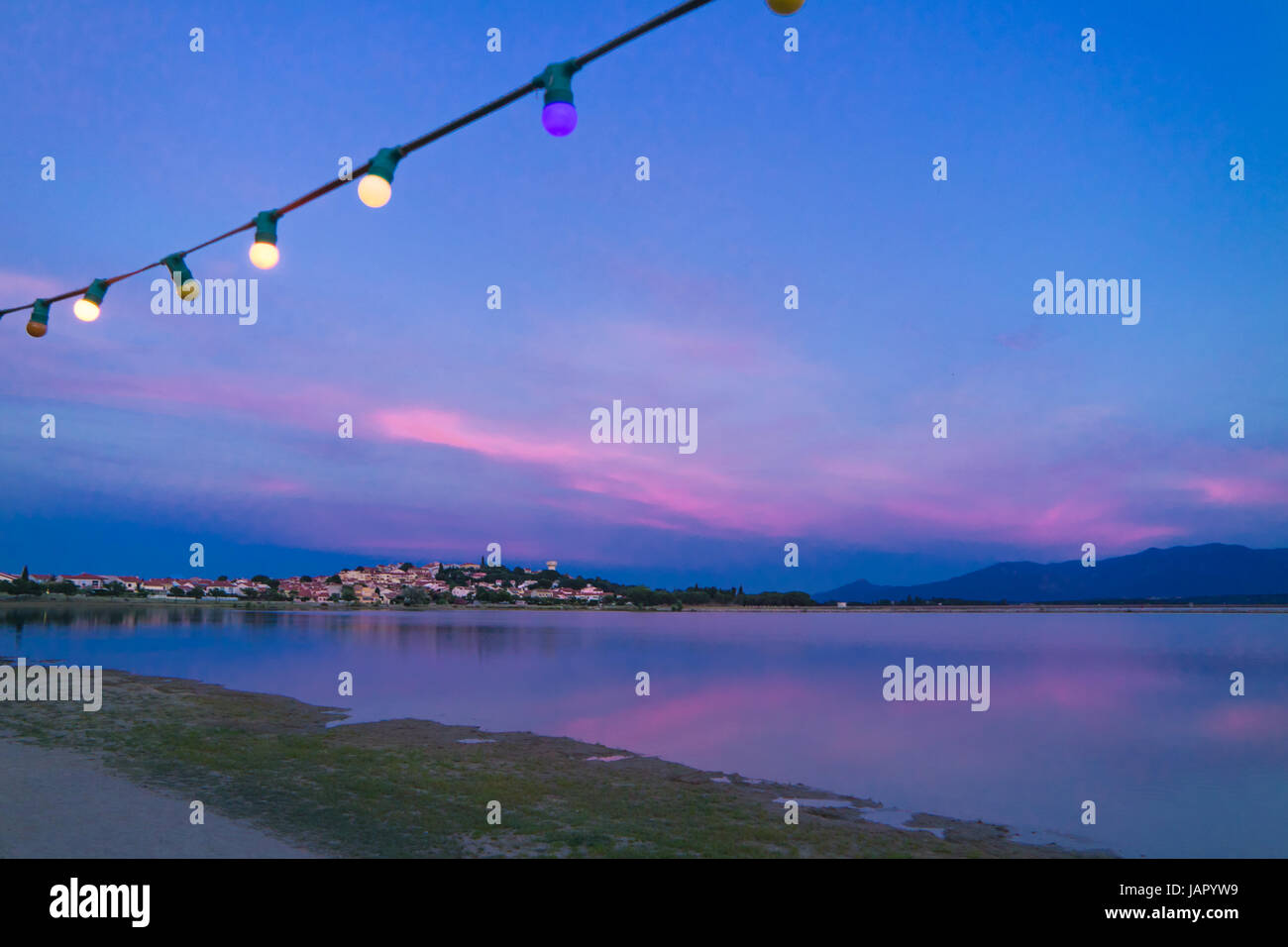 Festive outdoor electric light bulbs under blue sky at dusk in front of a french village and lake Stock Photo
