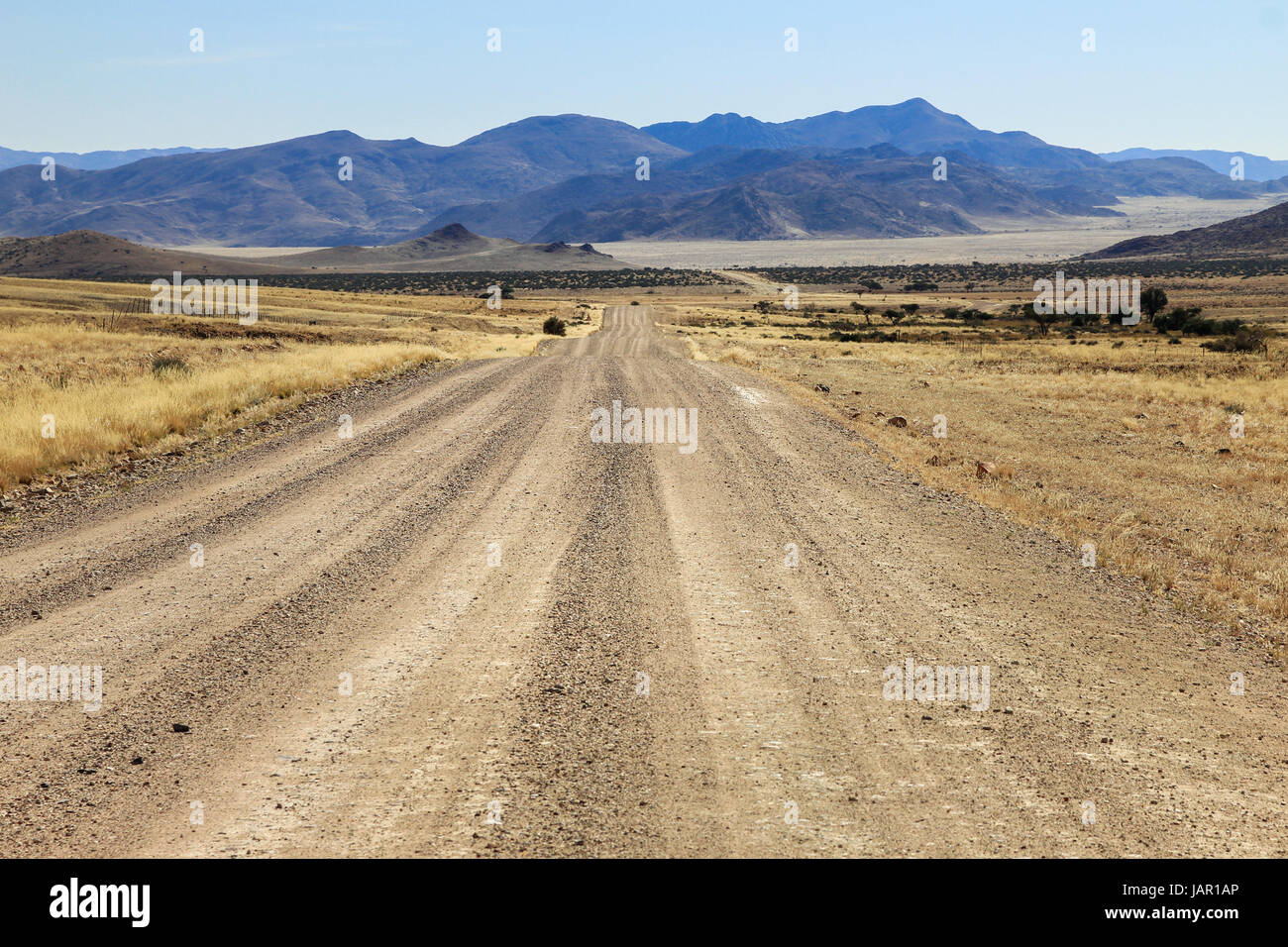 Bumpy road to mountains and through dry desert grassland. Stock Photo