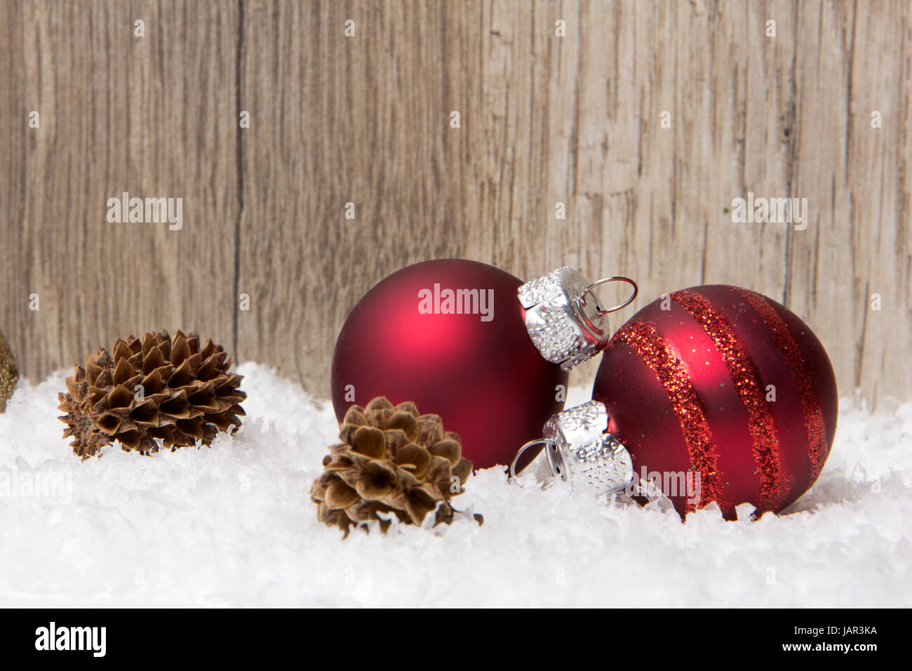 Weihnachten, Dekoration mit Holzhintergrund, Schnee, Weihnachtskugeln rot und Tannenzapfen Stock Photo