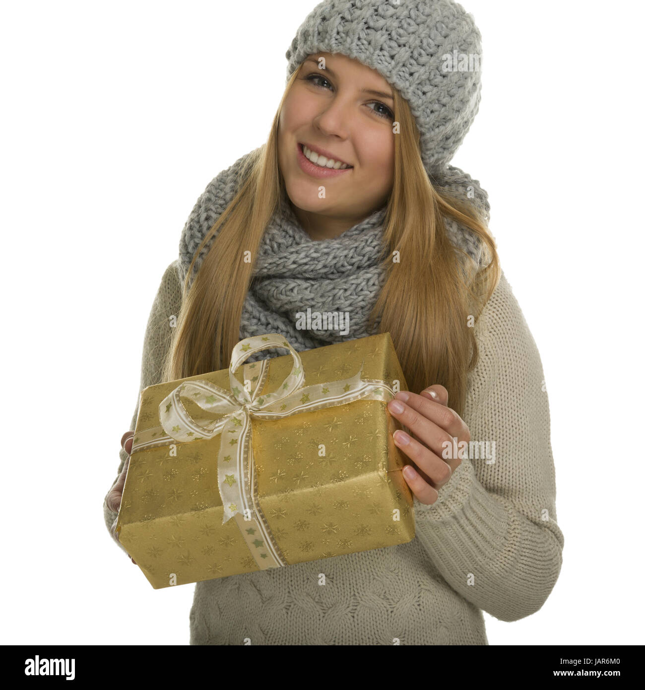 Frau mit langen Haaren in warmer Winterkleidung trägt ein golden verpacktes Weihnachtsgeschenk zwischen den Händen und ist fröhlich Stock Photo
