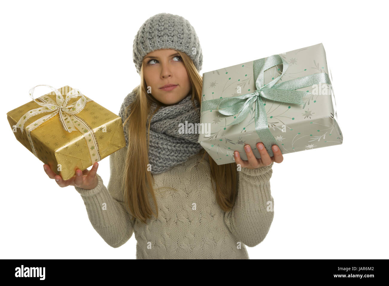 Frau mit langen Haaren und warmer Winterkleidung muss sich zwischen einem kleinen golden verpackten Geschenk und einem größeren grau und türkis verpacktem Geschenk entscheiden. Stock Photo