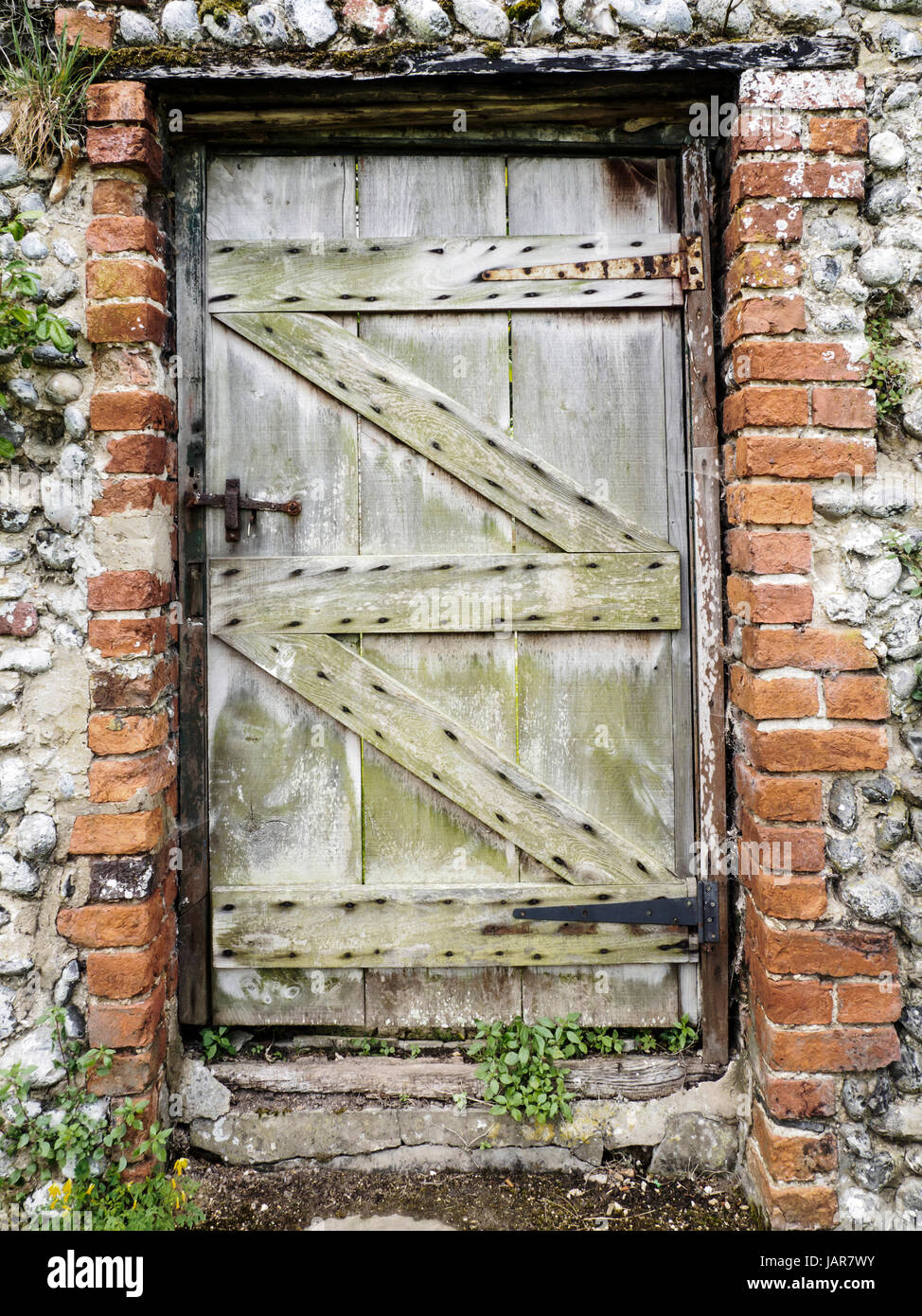 Old wooden doors in brick and flint walls in a a rustic garden in Norfolk, England. Stock Photo