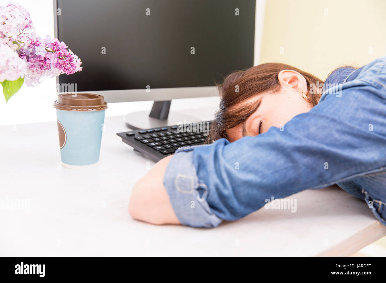 Young pretty woman tired and exhausted of work lying on table in front of computer and taking a break Stock Photo