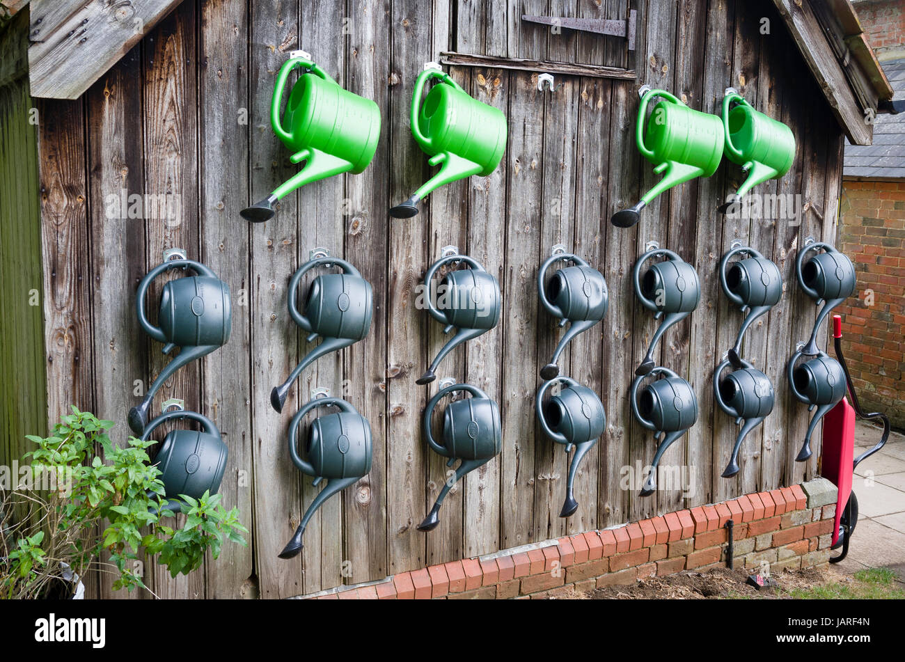 On a non-school working day the watering cans are stored neatly on the end of old building in UK Stock Photo