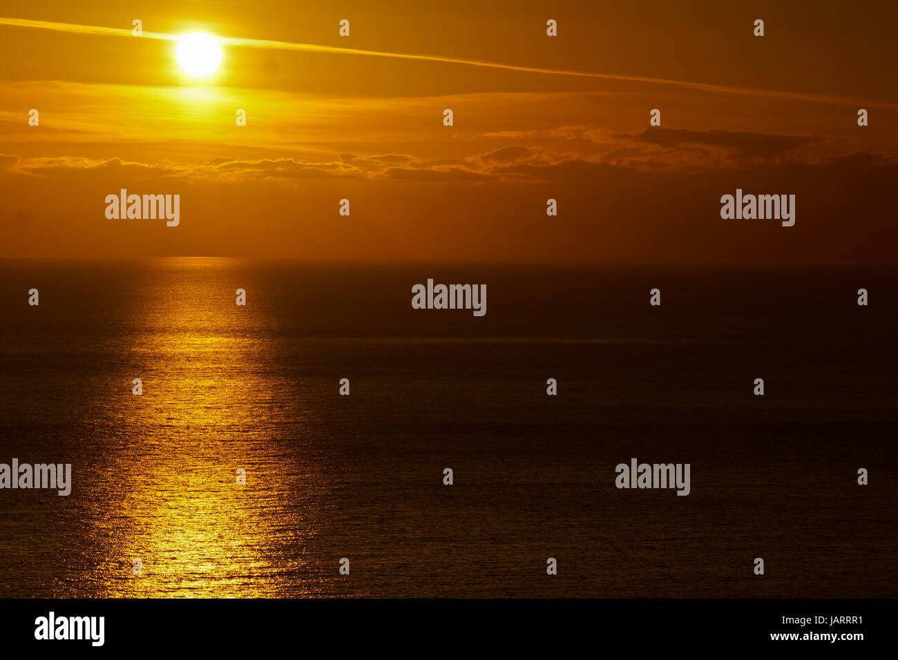 The sun sets over Portland, UK casting a wide golden glow over the sea ...
