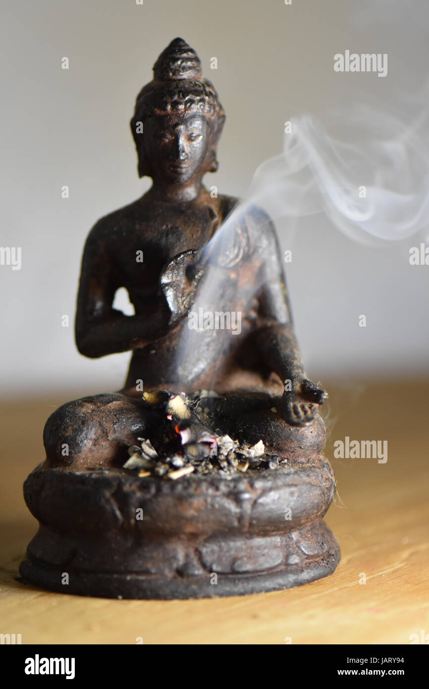 An offering of incense flame and smoke swirls around a brass buddha statue Stock Photo Alamy