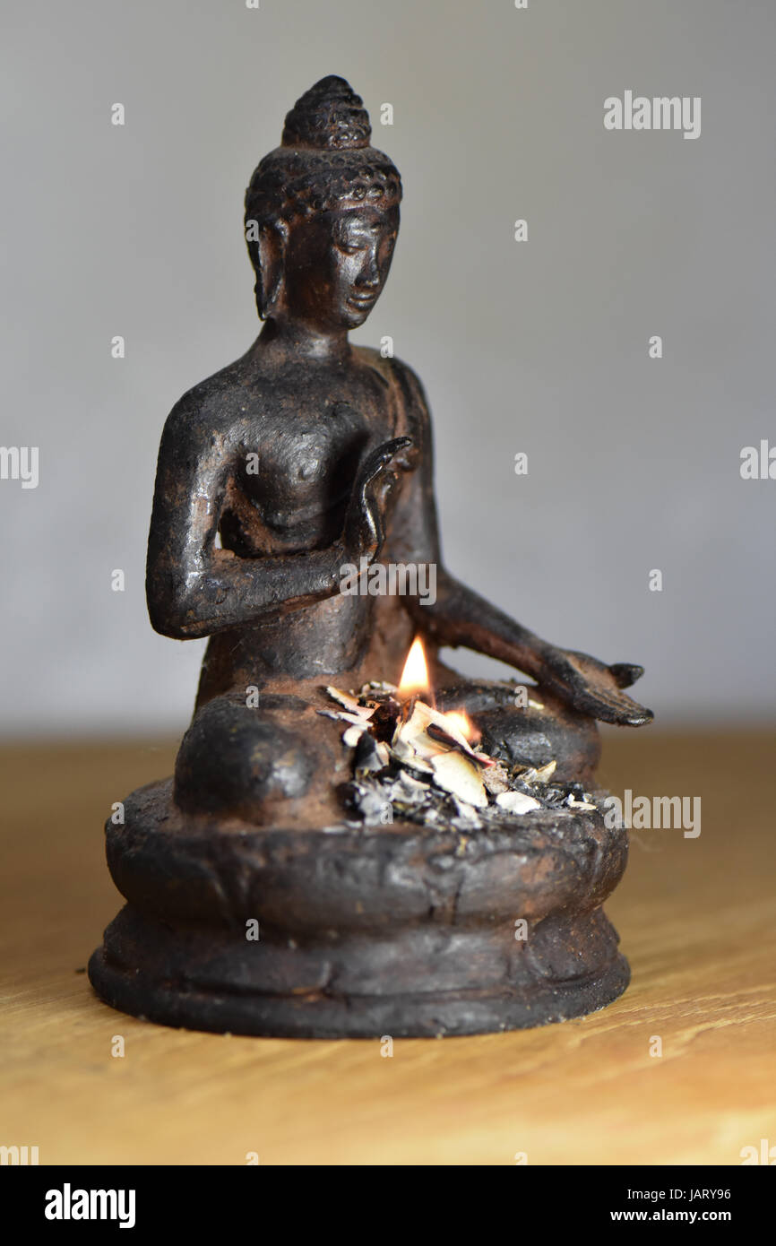 An offering of incense flame and smoke swirls around a brass buddha statue Stock Photo Alamy