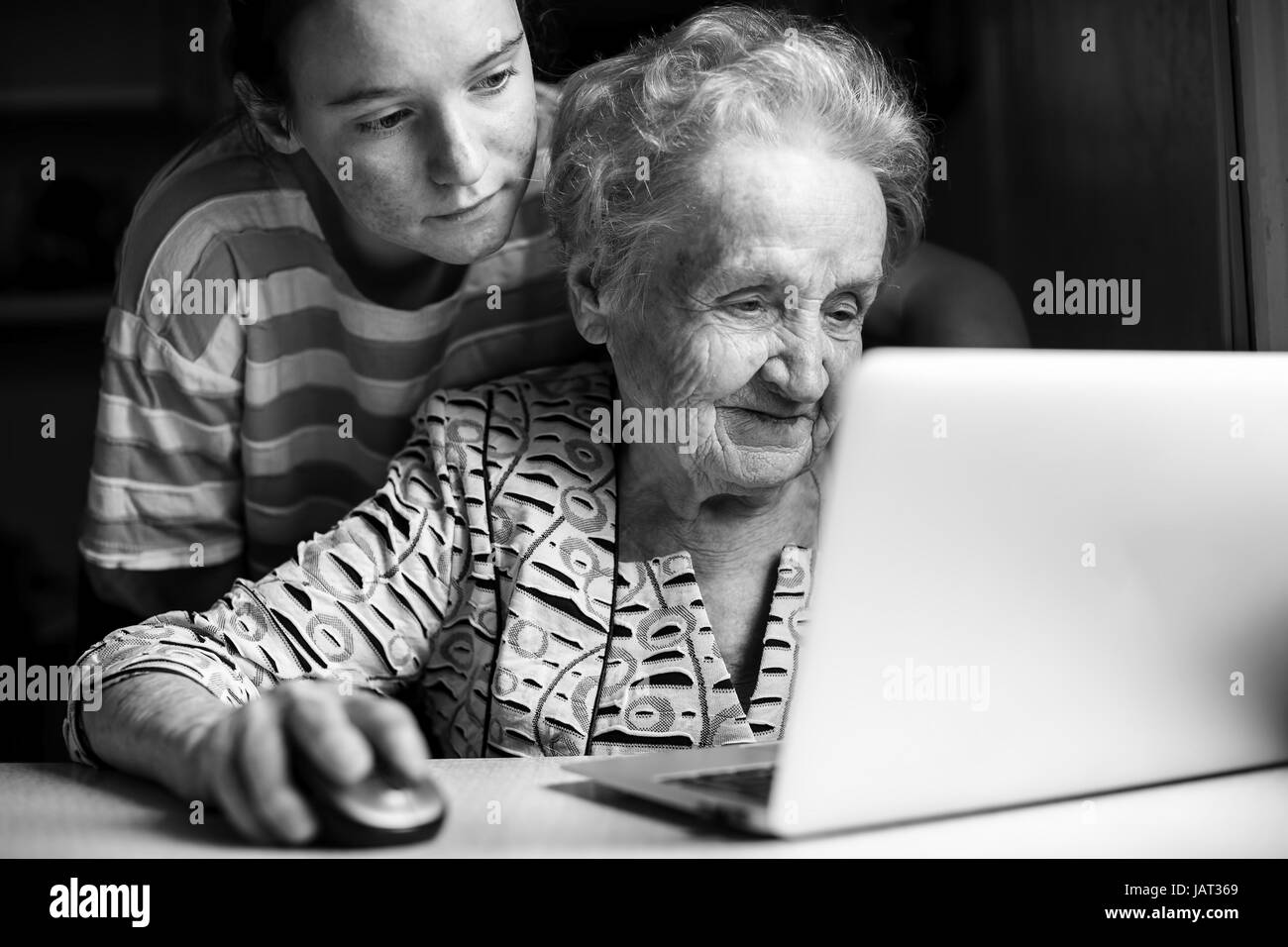 Girl teaches an elderly woman working on a laptop. Black-and-white photo. Stock Photo