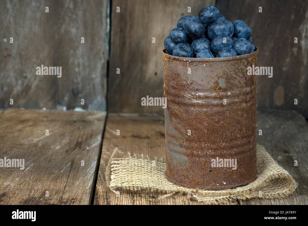 blueberries in rusty tin can on burlap and rustic wood Stock Photo