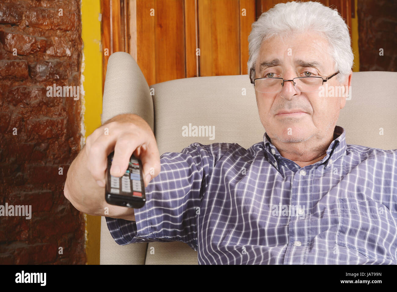 Portrait of an old man using remote control and watching tv. Indoors. Stock Photo