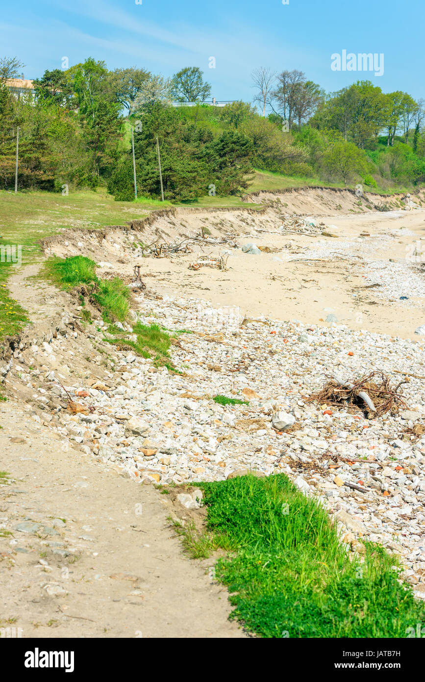 Beach erosion. Erosion has removed large parts of the soil into the sea, leaving stones and steep shorelines. Stock Photo