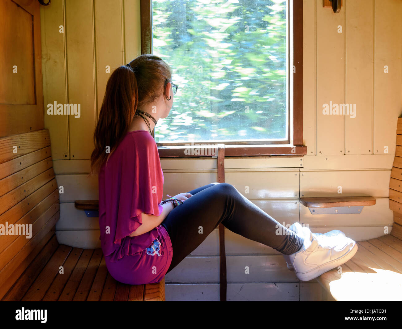 A girl sitting alone in an old train with wooden benches looking out from the window Stock Photo