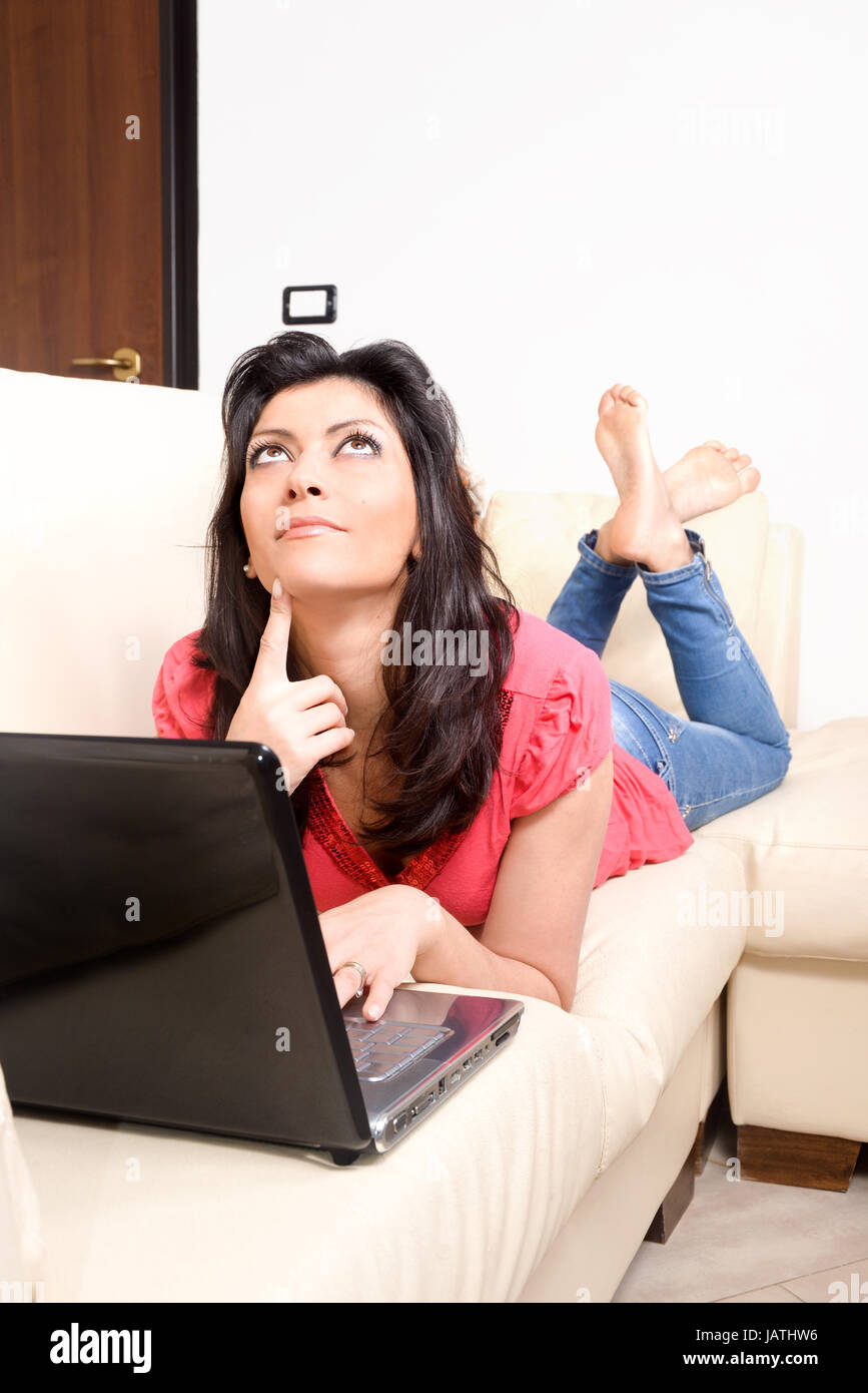 smiling young woman lying on the couch, surfing the internet with her laptop computer. Concept of relaxation Stock Photo