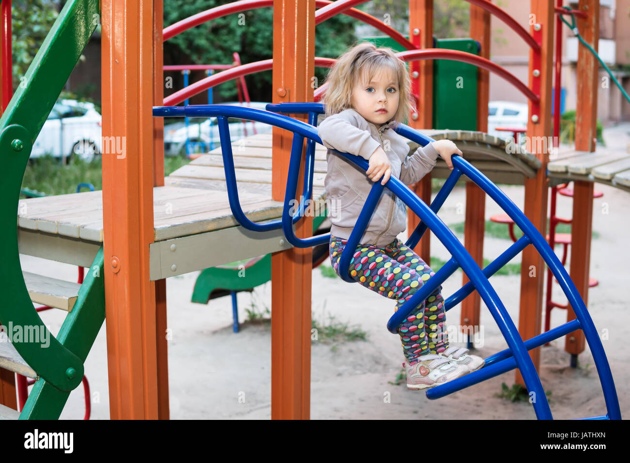 Little serious girl is sitting on the stairs on the children playground, close-up Stock Photo