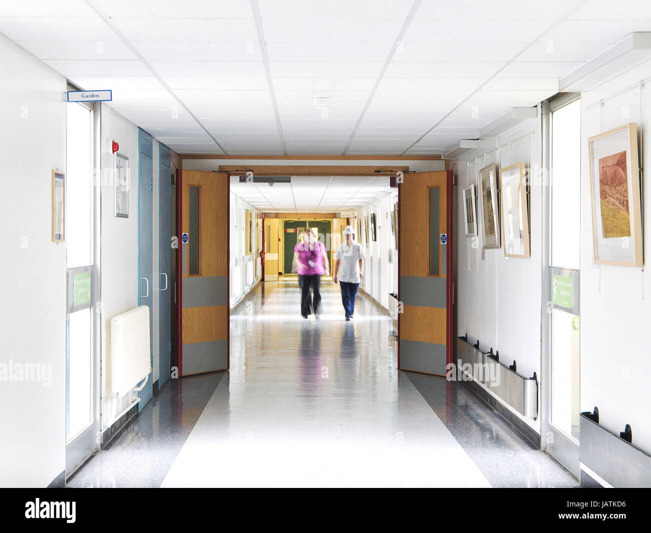 Empty UK NHS hospital corridor view, showing patients walking blurred in distance with NHS medical staff also walking towards camera Stock Photo