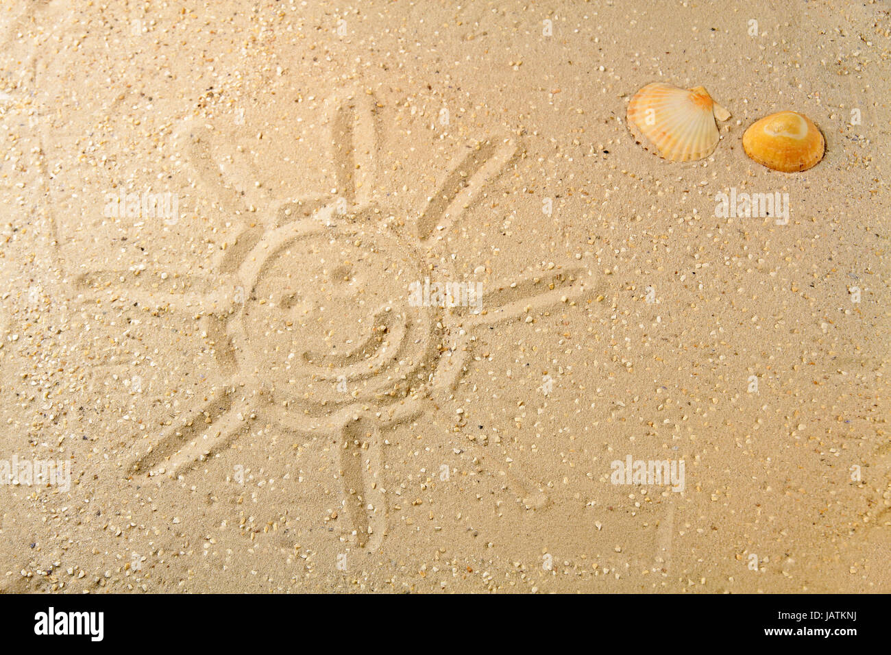 Sonne im Sand gezeichnet mit zwei farbigen Muscheln am Strand Stock Photo