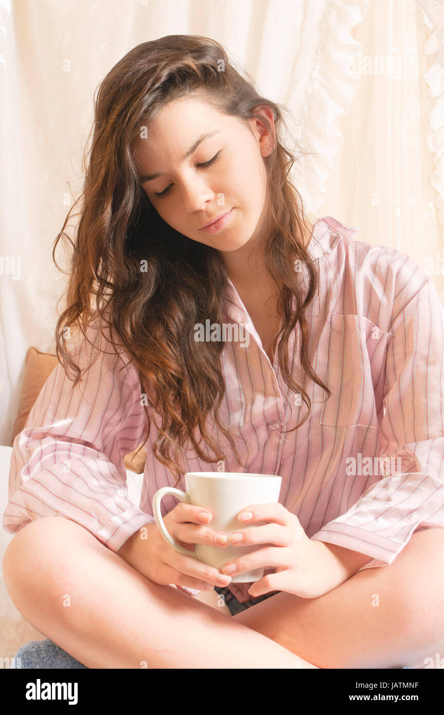 Junges Mädchen mit langen brünetten Haaren im Schlafanzug räkelt sich am Sonntagmorgen im Himmelbett. Stock Photo