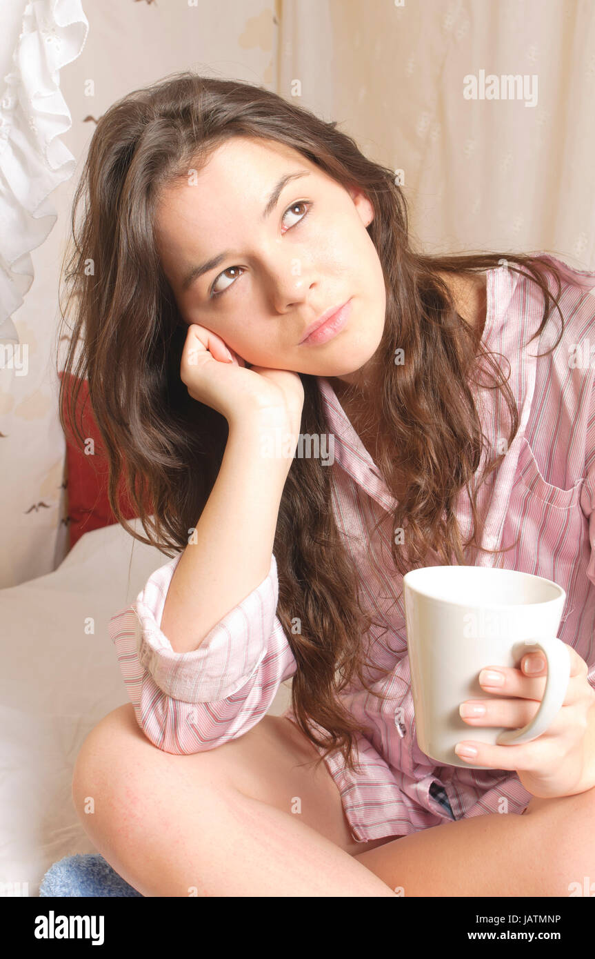 Junges Mädchen mit langen brünetten Haaren im Schlafanzug räkelt sich am Sonntagmorgen im Himmelbett. Stock Photo
