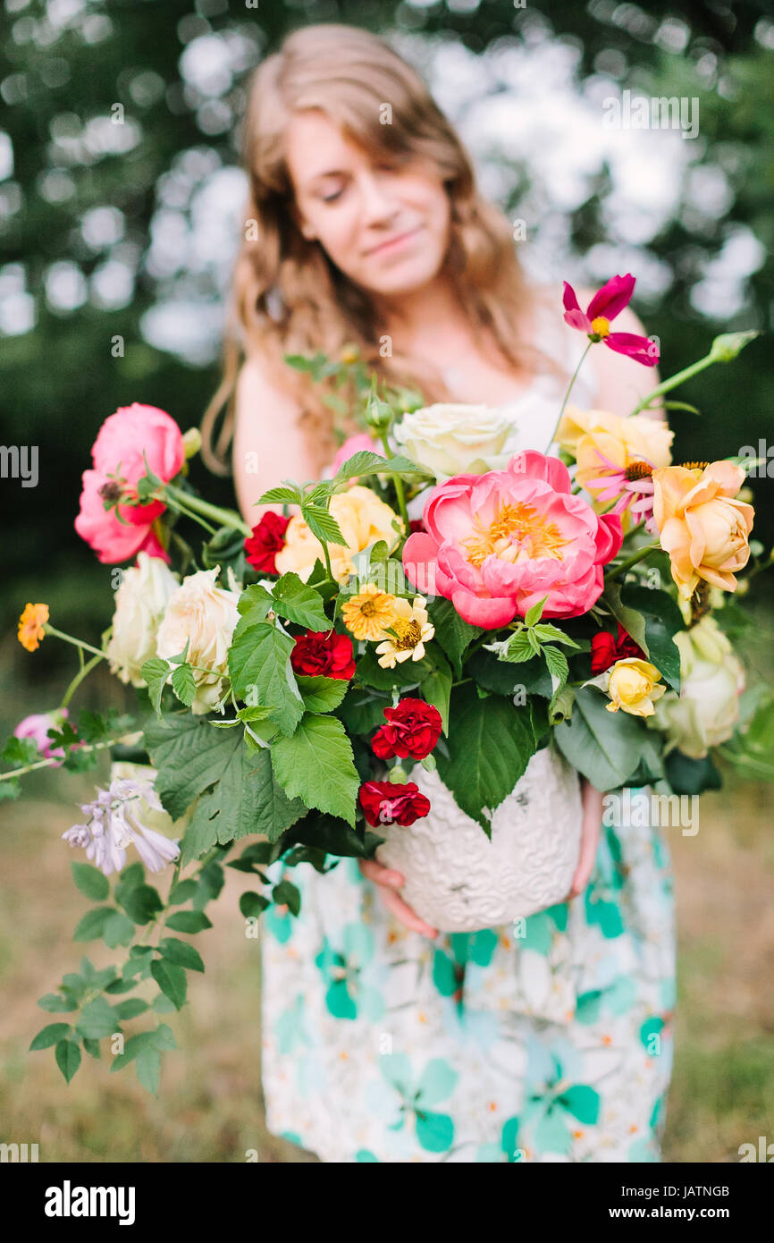 floral design, wedding, decoration, occasion concept - pretty woman in summer dress puting out grand bouquet of various flowers: big pink peonies, ten Stock Photo