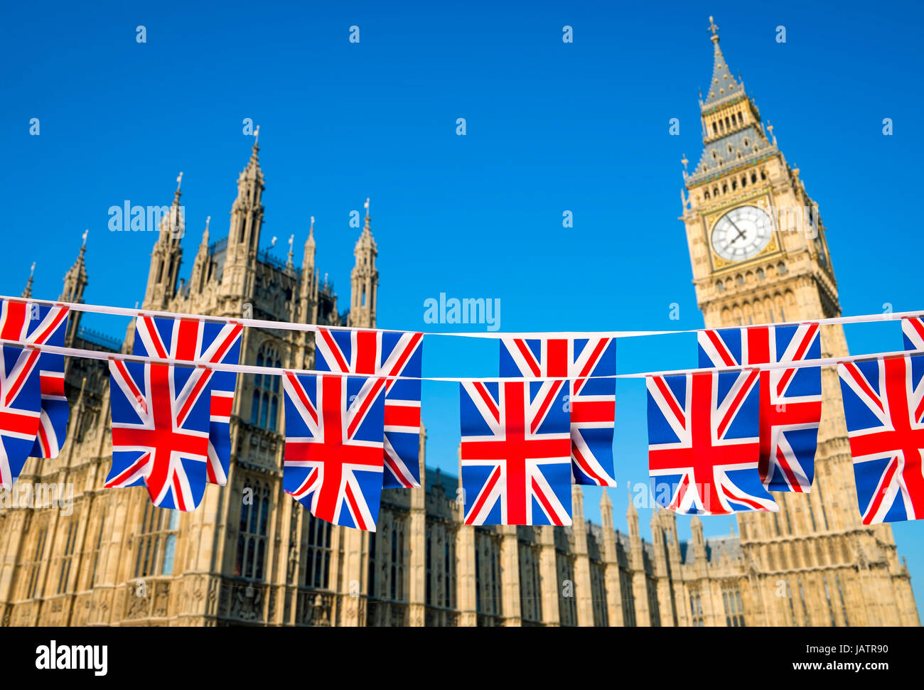 Two rows of Union Jack bunting flying in front of the Houses of Parliament at Westminster Palace with Big Ben under bright blue sky in London, England Stock Photo