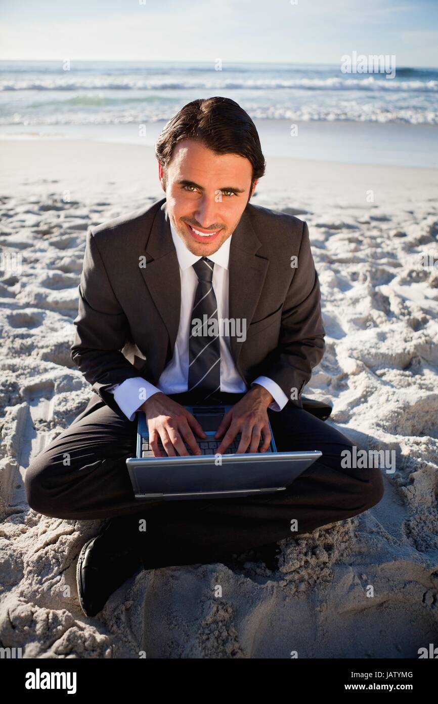Smiling businessman sitting cross-legged in front of the sea with a ...