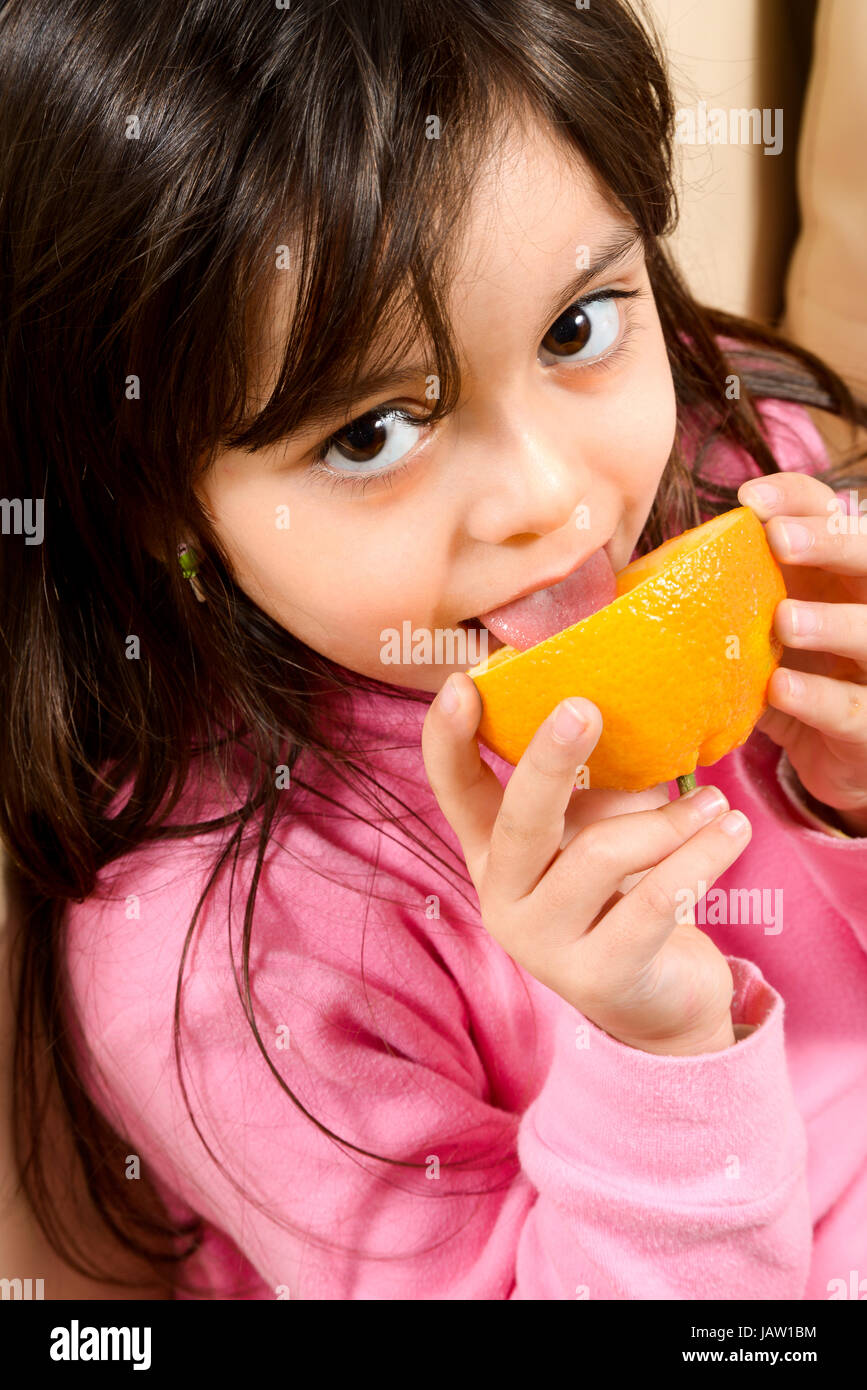 Caucasian baby girl with dark hair, eat an orange. Concept of healthy food Stock Photo