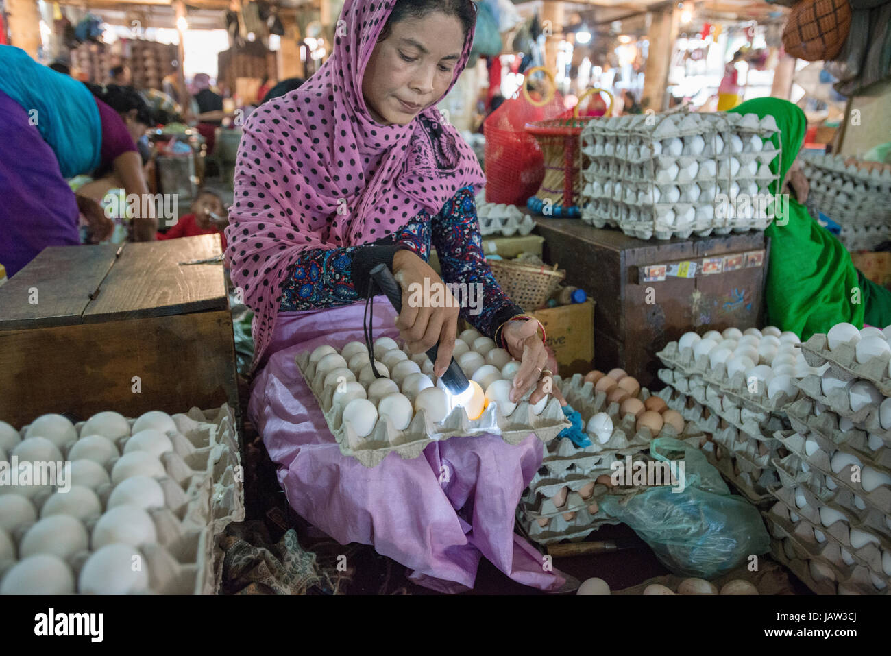 A market trader checks the condition of her eggs with a torch at an indoor market stall in Imphal, Manipur, India Stock Photo