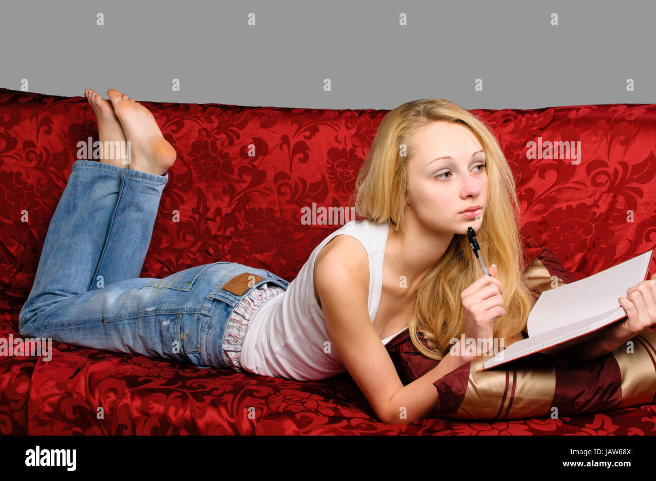 Junges hübsches Mädchen mit langen blonden Haaren liegt zuhause auf dem Sofa und schreibt in ihr Tagebuch. Stock Photo