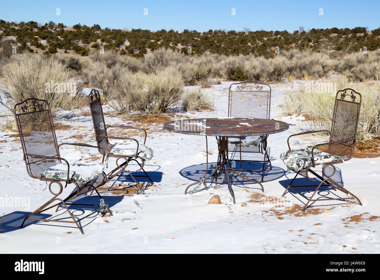 Four empty garden chairs around a table in the desert with snow Stock