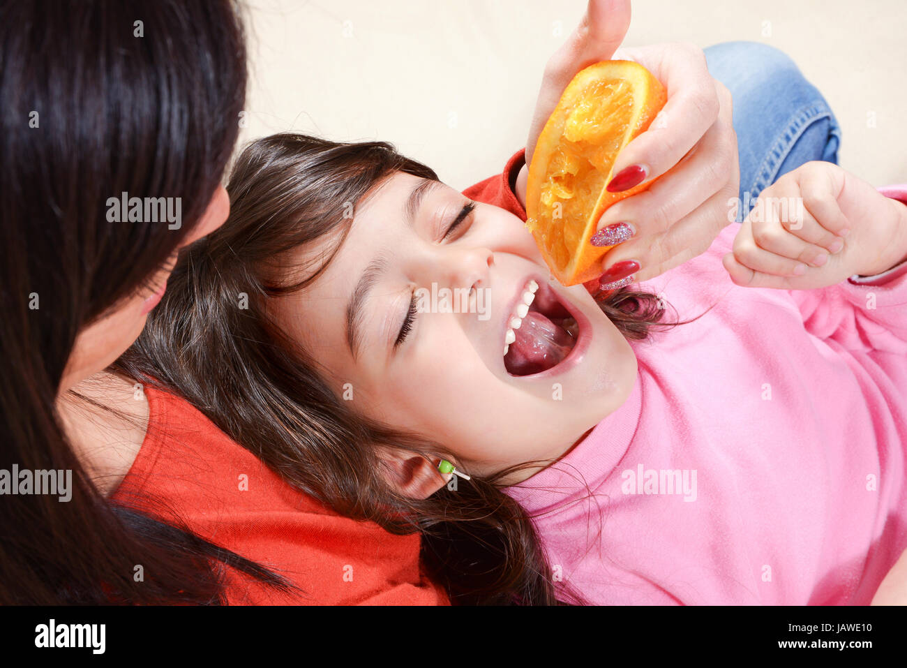 Caucasian baby girl with dark hair, drinking juice direct from an orange. Concept of healthy food Stock Photo