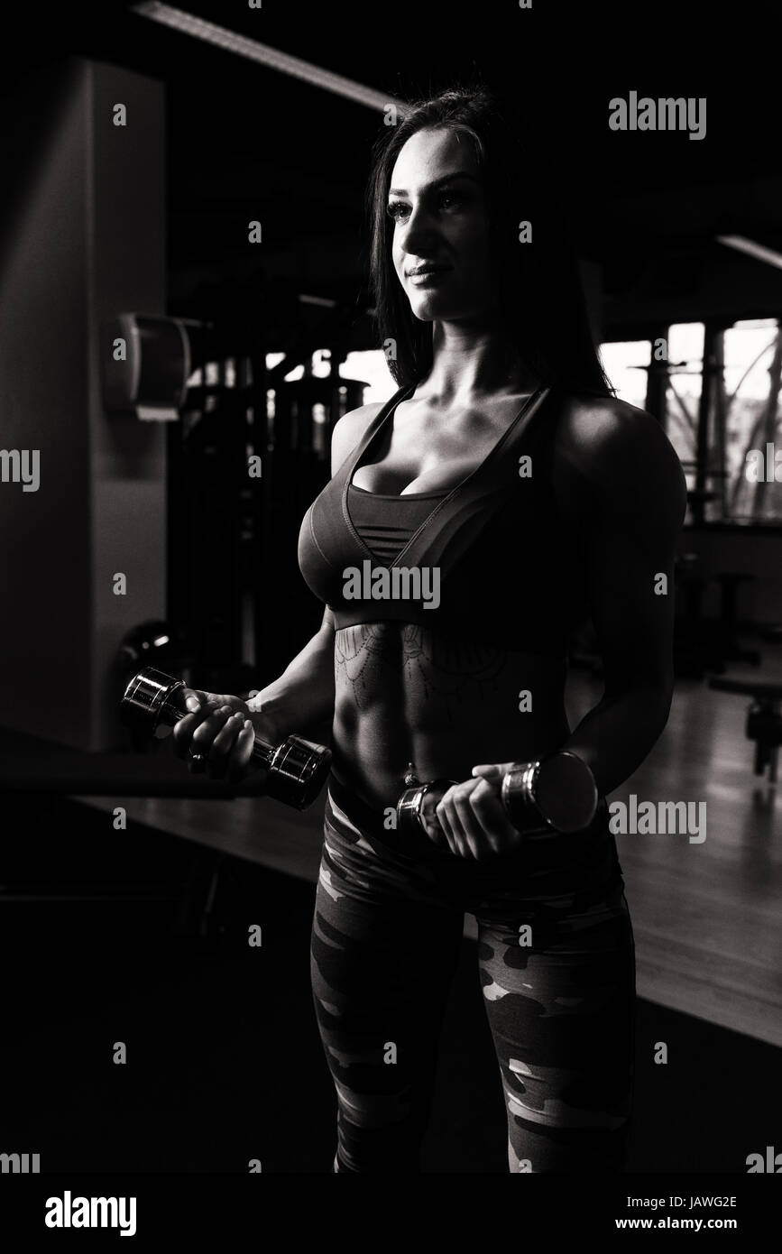 Young Woman Working Out Biceps In A Gym - Dumbbell Concentration Curls Stock Photo