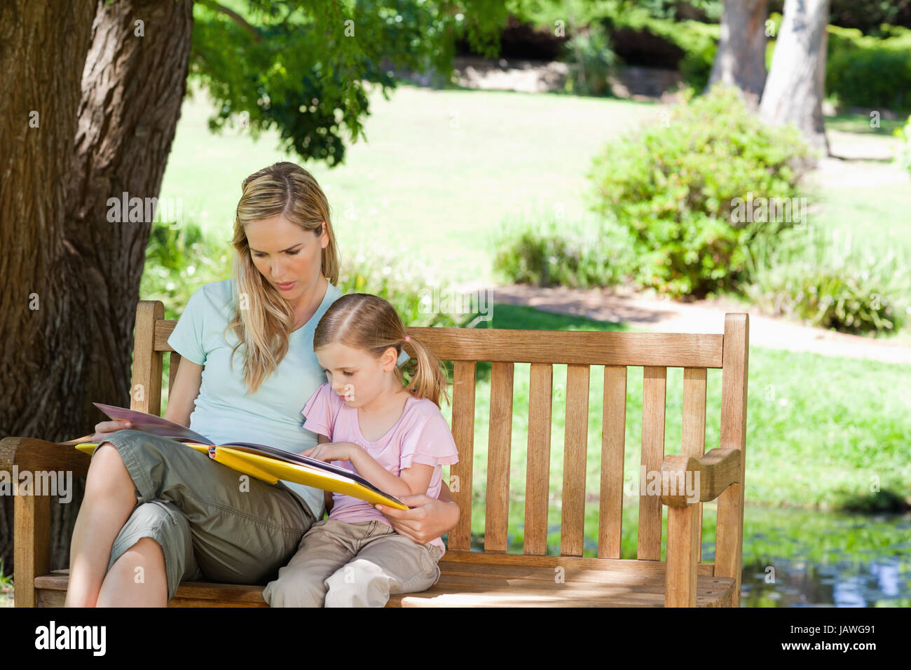 A mother and her daughter sit on the park bench and read Stock Photo ...