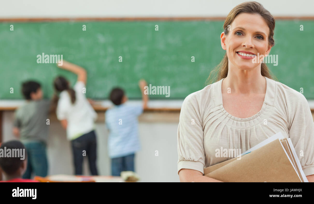 Smiling teacher with students on blackboard behind her Stock Photo - Alamy