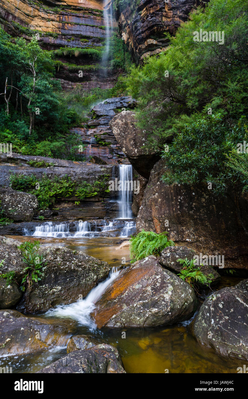 A curtain of mist and waterfalls cascades from a sandstone cliff into rock pools. Stock Photo