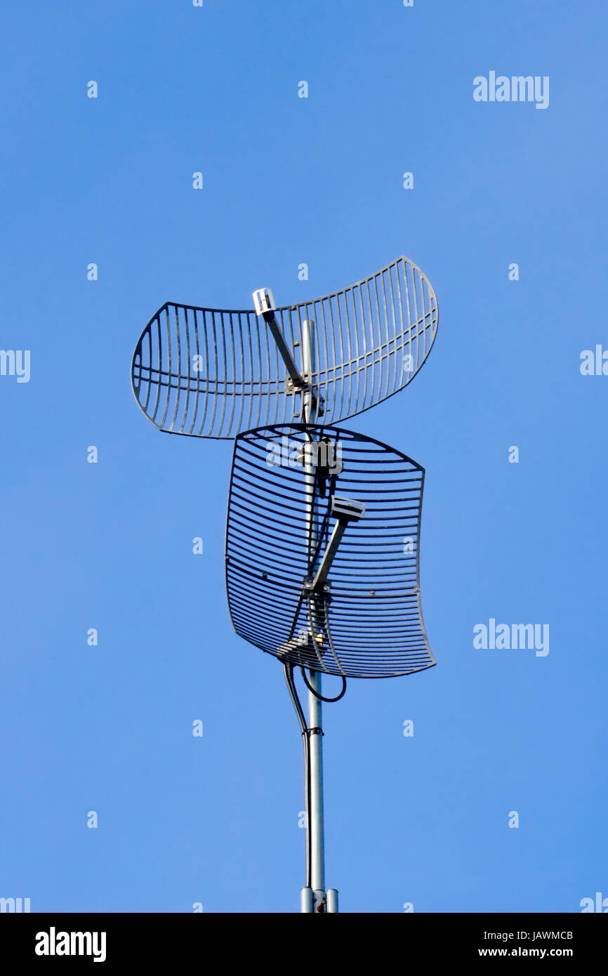 Two curved dish antennas pointing in different directions on blue sky