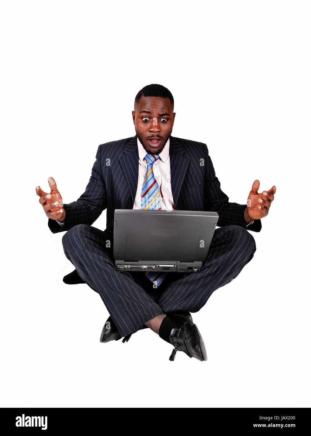 A black businessman sitting on the floor with a laptop on his lap and ...