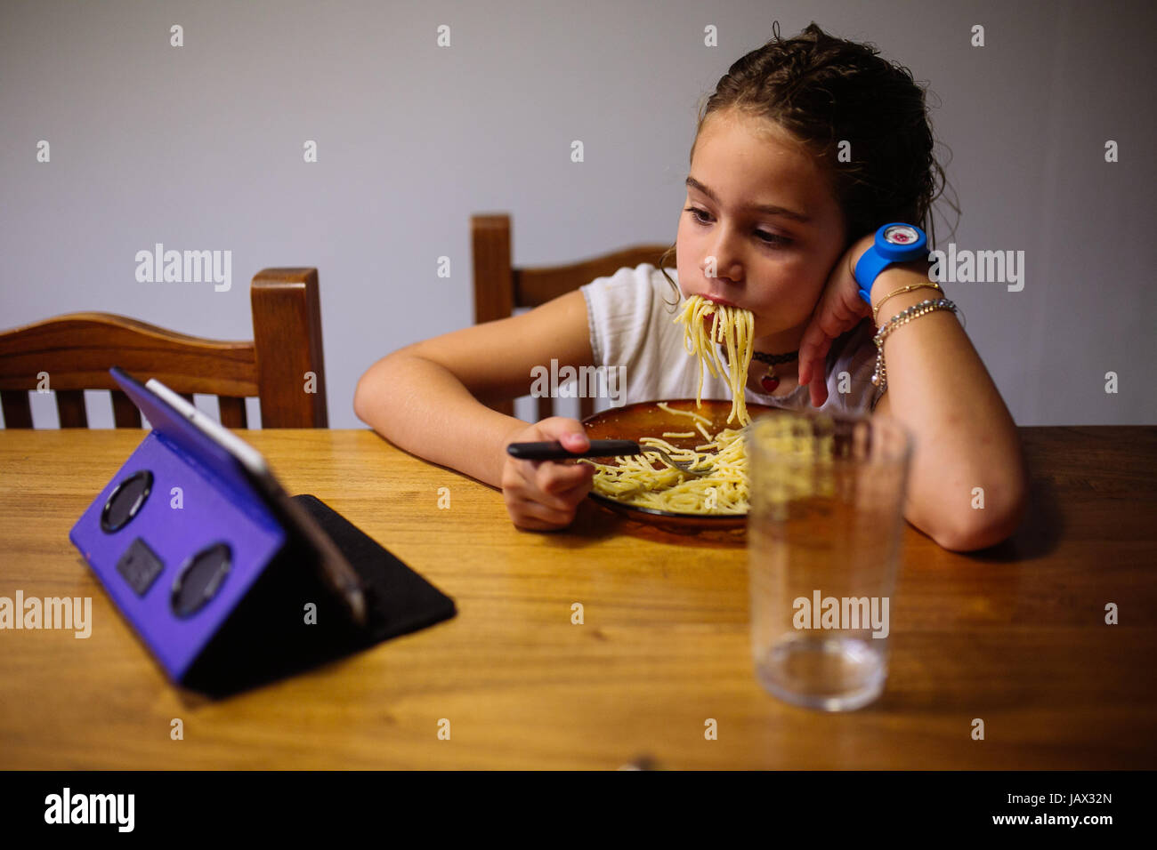 Young girl eating spaghetti pasta rudely while watching a tablet Stock Photo