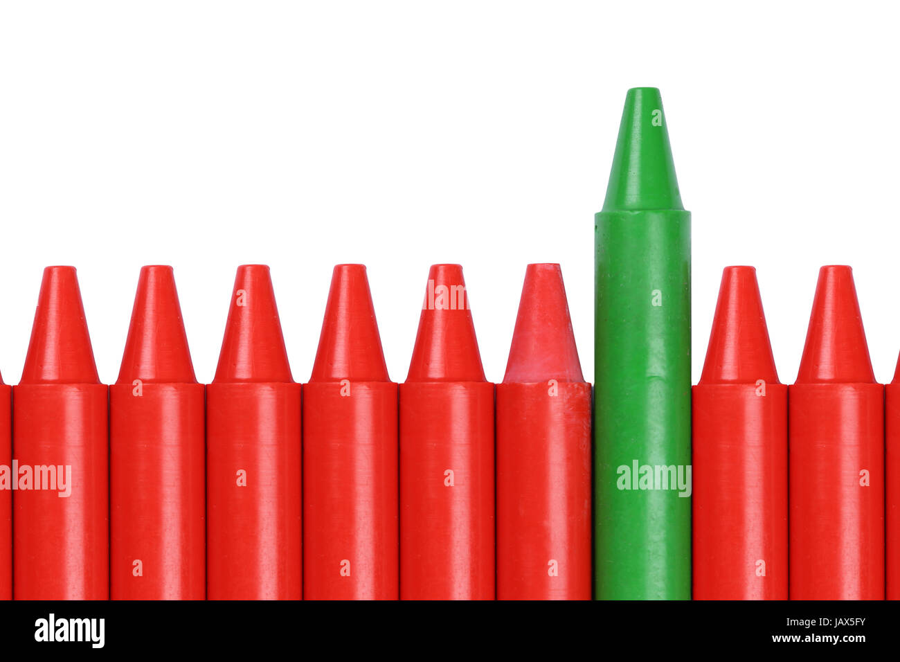Ein grüner Wachsmalstift ragt aus einer Reihe roter Buntstifte heraus Stock Photo