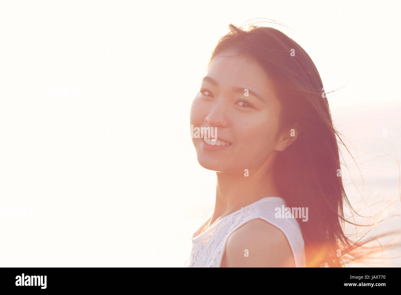 Young Japanese woman in a white dress at a cliff over the sea at sunrise, Chiba, Japan Stock Photo