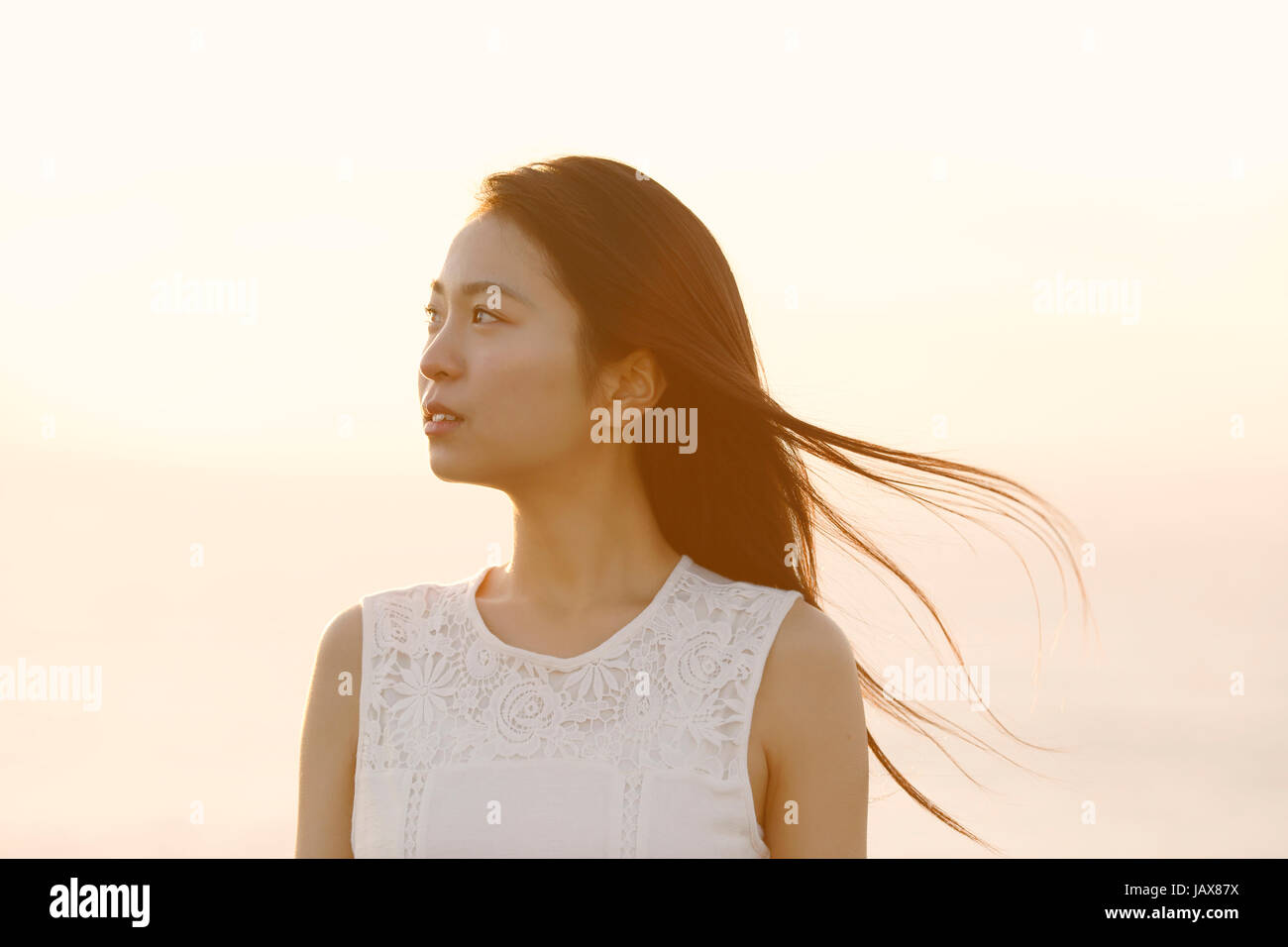 Young Japanese woman in a white dress at a cliff over the sea at sunrise, Chiba, Japan Stock Photo