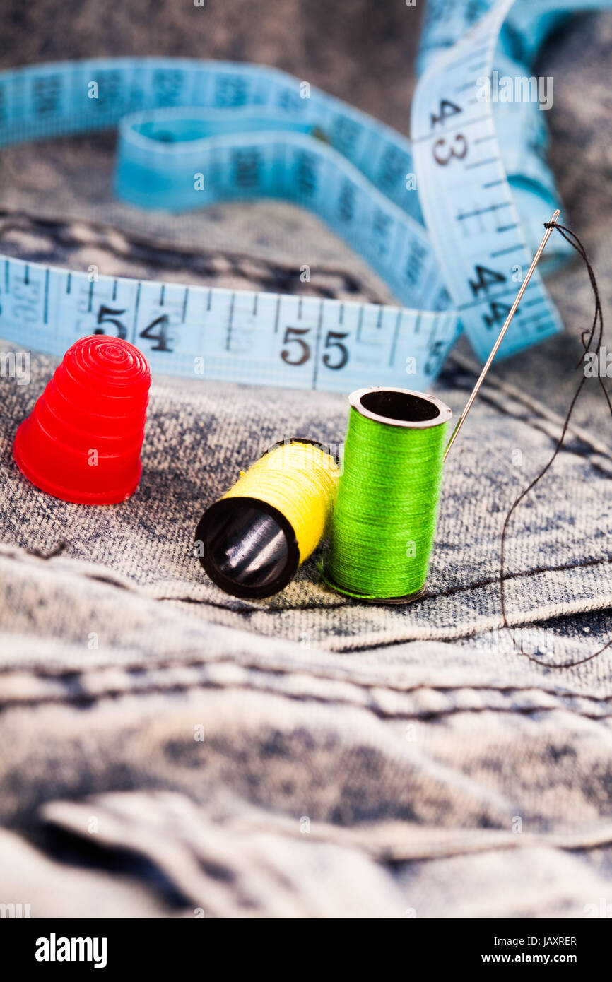 Needle, two colourful reels of cotton, a thimble and a tape measure on  denim cloth for sewing, alterations or repair Stock Photo - Alamy