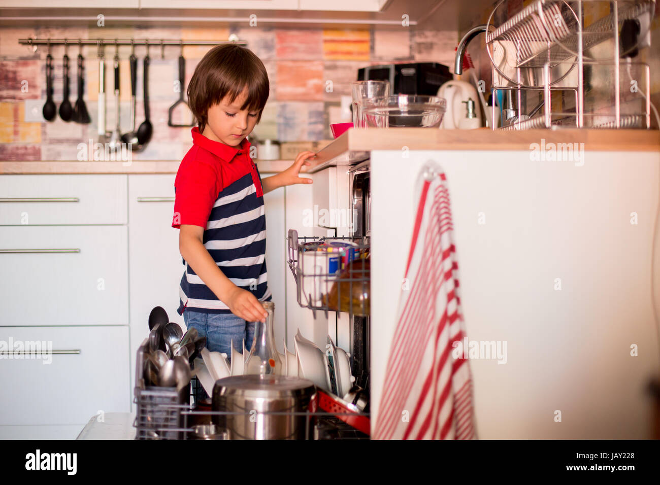 Preschool child, boy, helping mom, putting dirty dishes in dishwasher at home, modern kitchen Stock Photo
